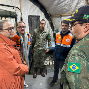 Secretaria da Saúde em Guaíba após enchentes 2024. Arita conversa com um militar no hospital de campanha e é observada por outras quatro pessoas.